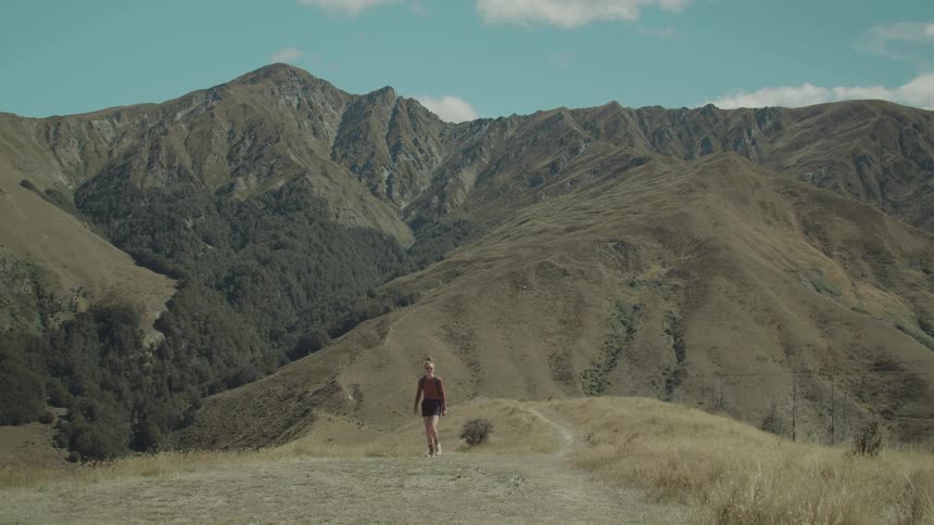 A hiker walks along a trail with a scenic mountain landscape in the background