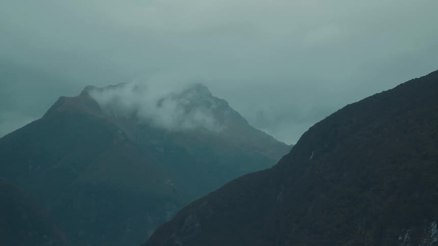 Dark mistshrouded mountains with clouds clinging to their peaks under a grey sky