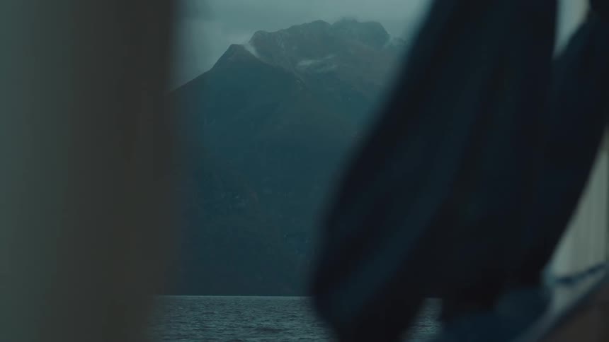 Towering dark mountains loom over a calm body of water under a misty blocked by objects in the foreground