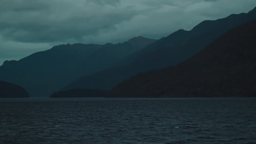 A mountain range on a large body of water on a cloudy day