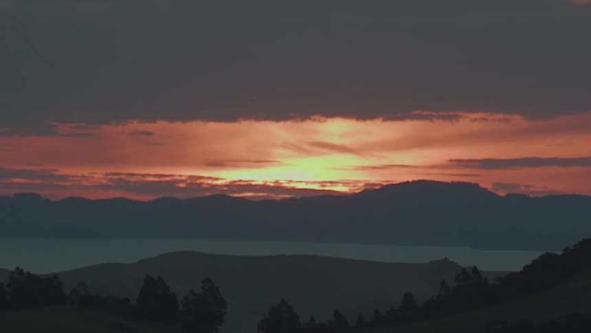 Sun setting on the horizon over the mountains across the lake