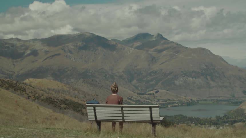 A woman sits on a bench to look at the mountain in the distnace