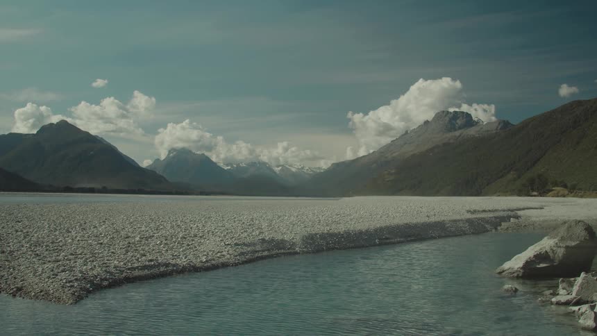 A serene river flows beside a stony riverbed with mountains in the background