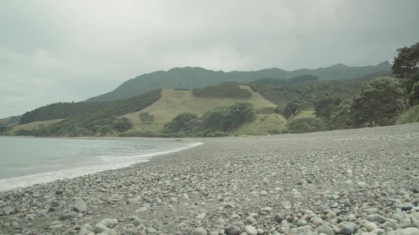 Rocky beach curving under cloudy sky with hills and mountains behind