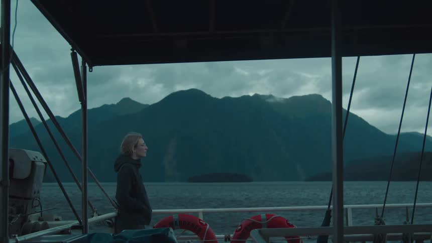 A woman standing on the outside of a boat watching nature then walking