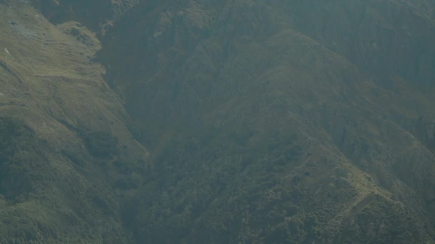 Aerial view of the rugged texture of a mountainside with varied vegetation covering its slopes under dim hazy light