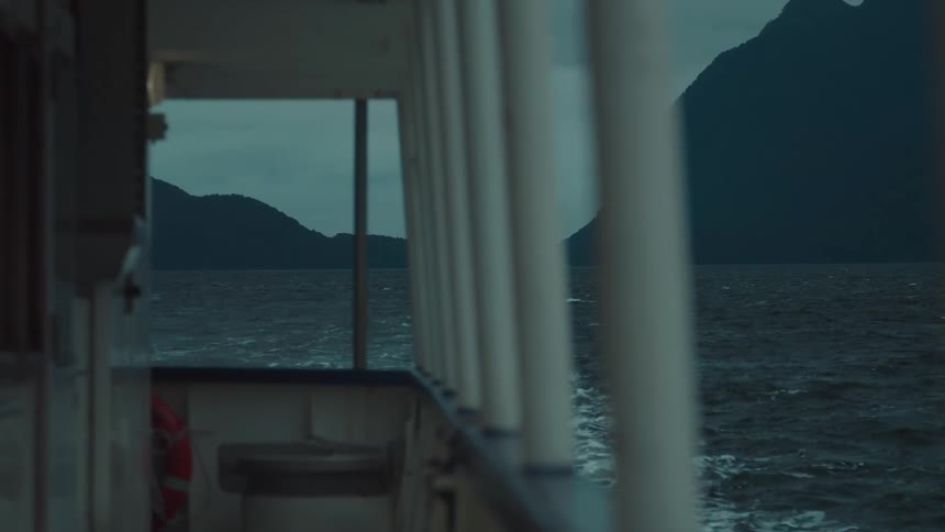 From the deck of a boat dark mountains rise from choppy water under an overcast sky
