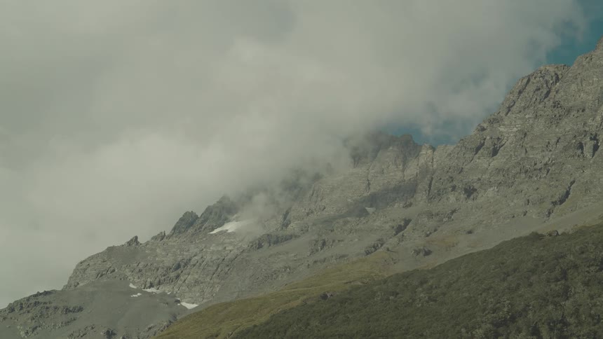 A mountain range with stone mountains with a thick white cloud passing over the top of them