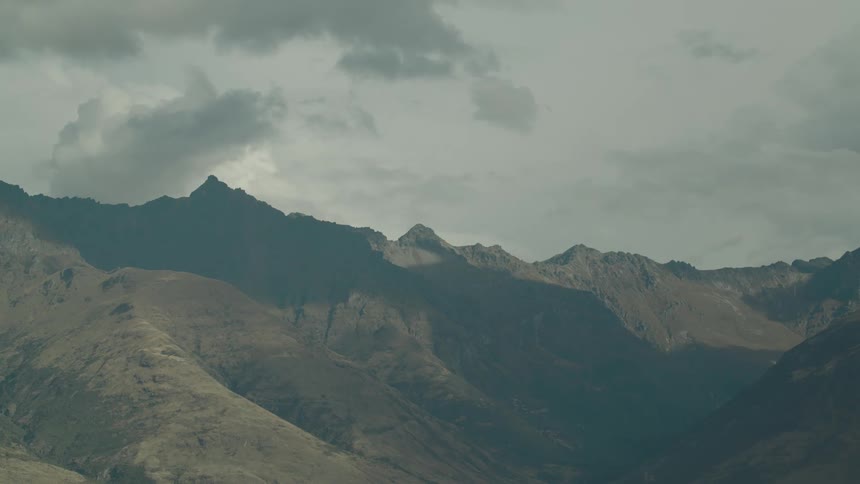A range of rugged mountains under a cloudy sky with shadows and light playing across their slopes