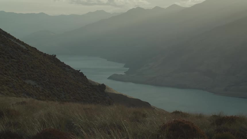 Fog obscures the mountains across the water from a grass covered slope