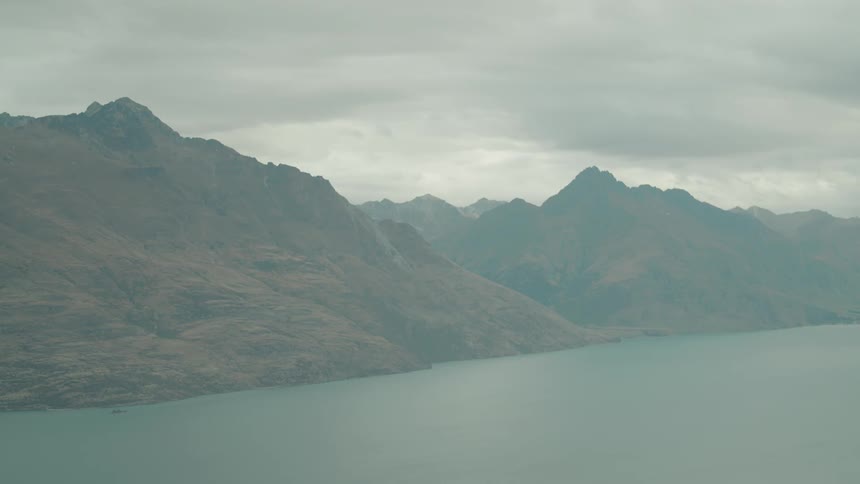 Vast mountains slope down to a wide ocean inlet under an overcast sky