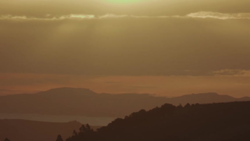 A sunset or sunrise over a series of rolling hills and mountains with the sky glowing in warm orange and yellow tones
