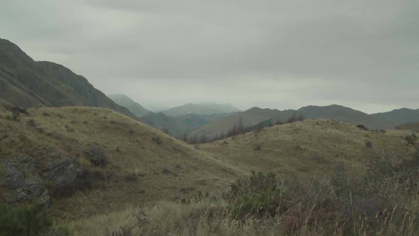 Rolling hills and distant mountains lie under a cloudy quiet sky