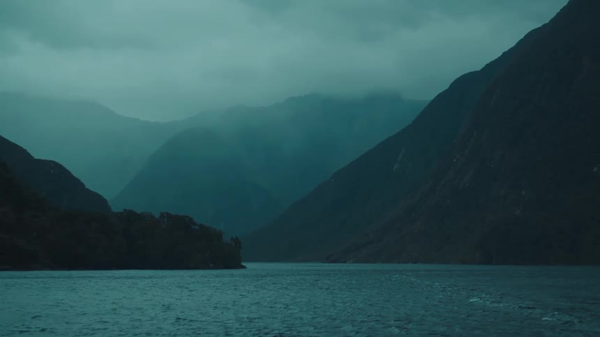 Dense fog covers the mountains bordering the water on an overcast day