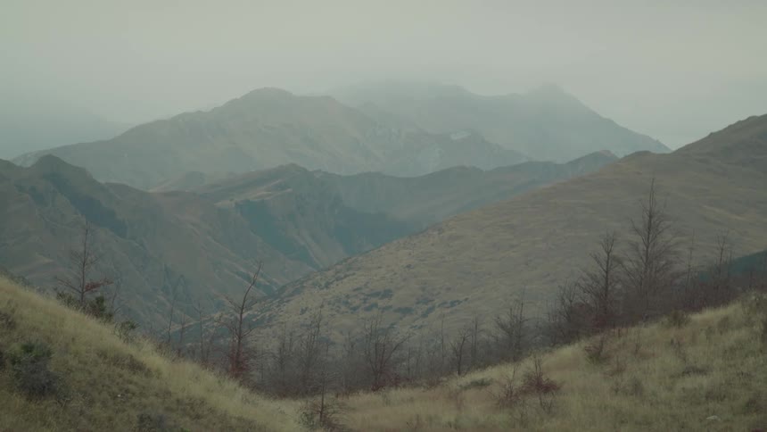 Foggy mountains with dry hills and bare trees under overcast skies