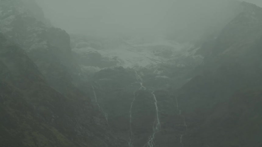 A foggy mountain landscape with waterfalls flowing down steep rocky slopes