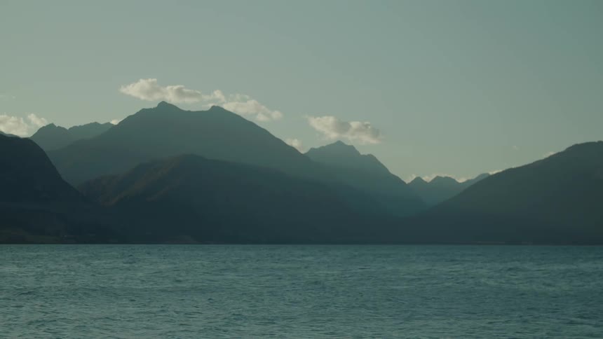 Silhouetted mountains rise beyond a calm lake under a clear sky with a few wispy clouds