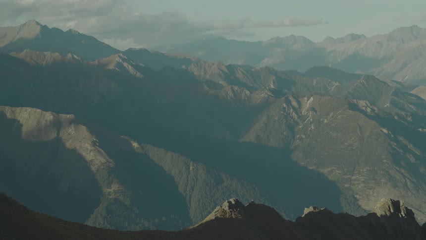 Light and shadows stretch over rugged mountain ridges under cloudy sky