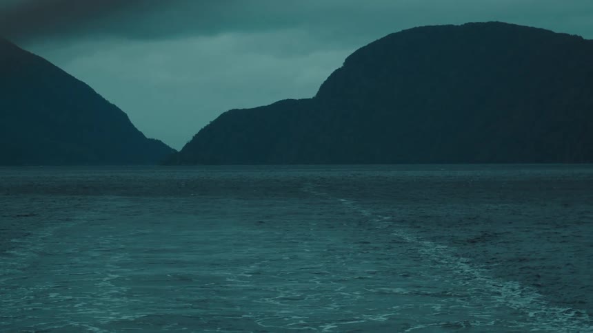 The surface of the sea water with some waves caused by a boat and with mountains in the background on a cloudy day