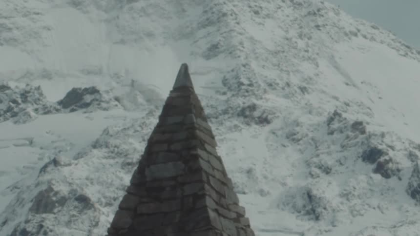 A triangular stone monument standing tall against a snowy mountainous backdrop under a grey sky