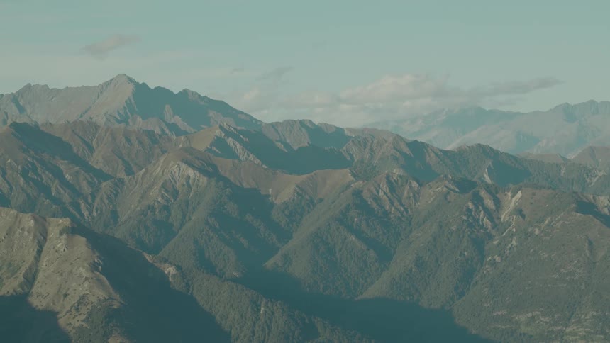 An aerial view captures an expansive mountain range with numerous peaks and valleys under a partly cloudy sky
