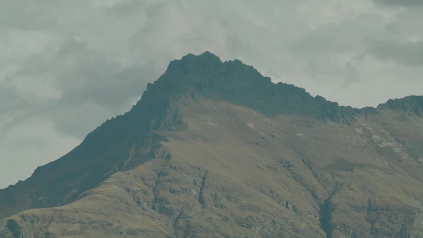 A rugged mountain peak stands prominently against a backdrop of an overcast cloudy sky