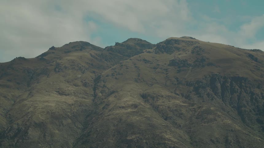 A rugged mountain range stands under a partly cloudy sky