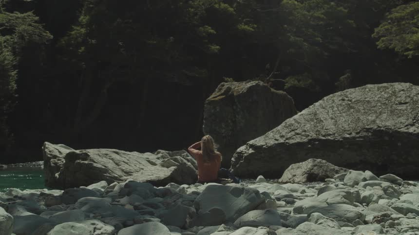 A woman sitting on rocks near a river with a forest in the background