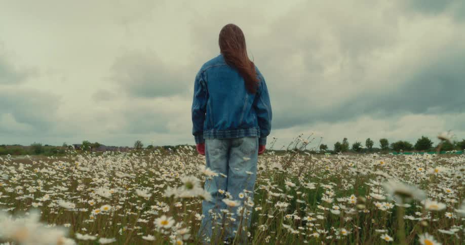 Woman stands backfacing in a grassy field with wildflowers