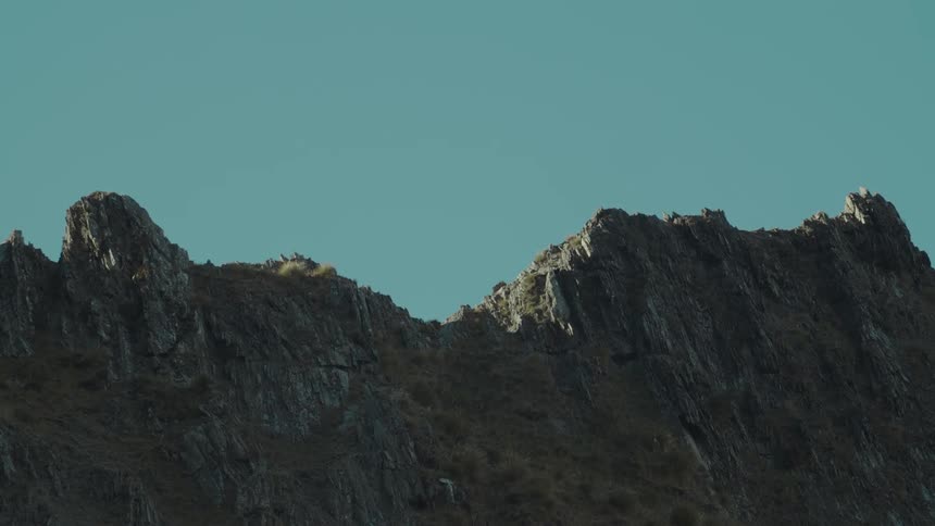The sunlit rocky ridgeline of a mountain with sparse vegetation stands out against a clear blue sky