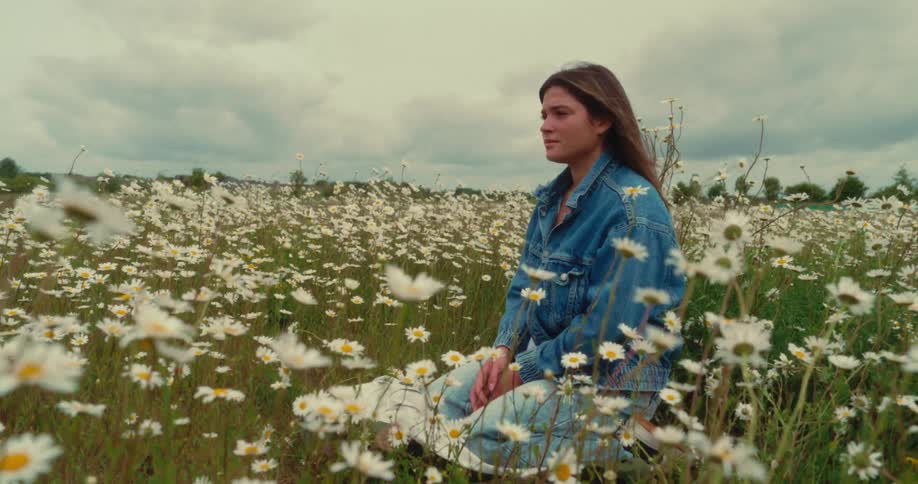 Woman sitting on a blanket in a meadow of daisies swaying in the wind