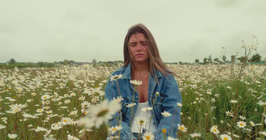 A young woman sits peacefully in a field of daisies eyes closed
