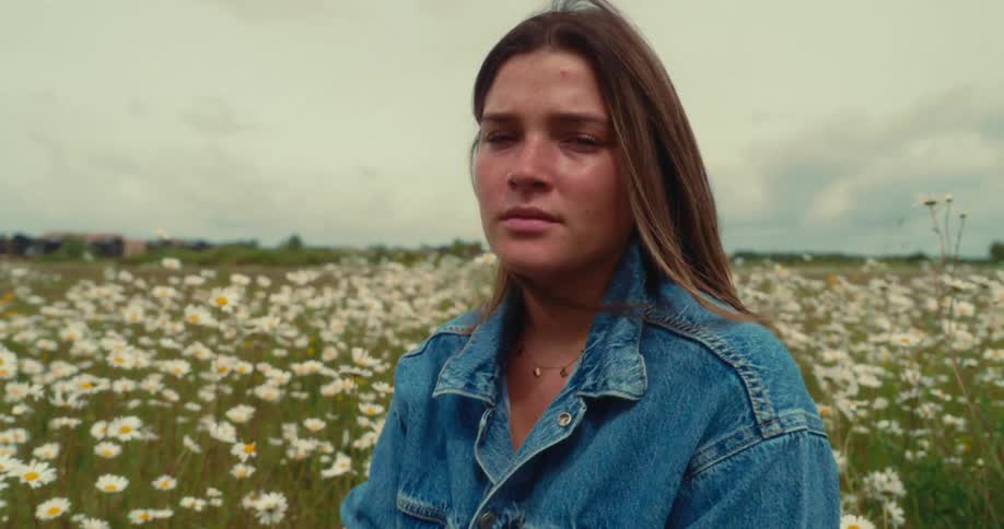 Woman sitting in a field among wildflowers brushes back her hair