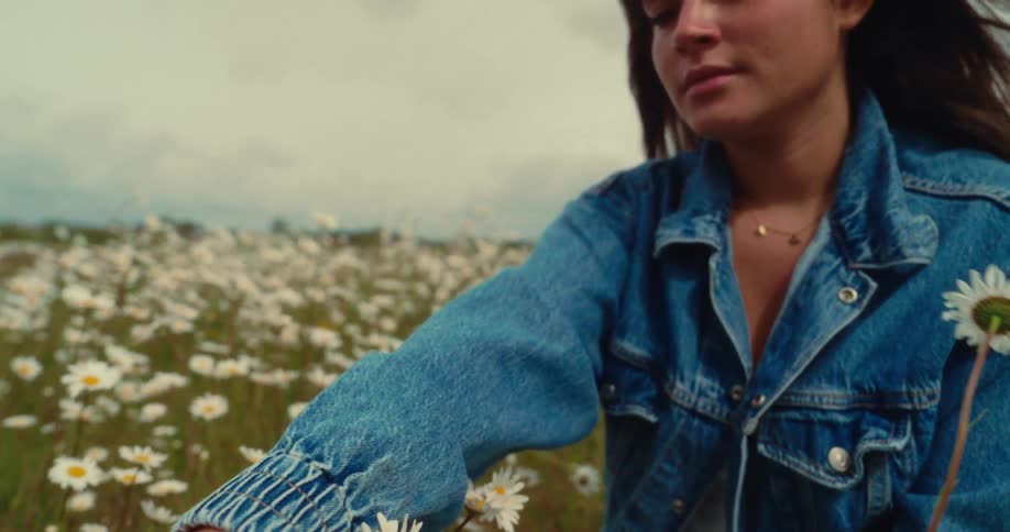 A woman gently brushes her hand through daisies in a wide flower field