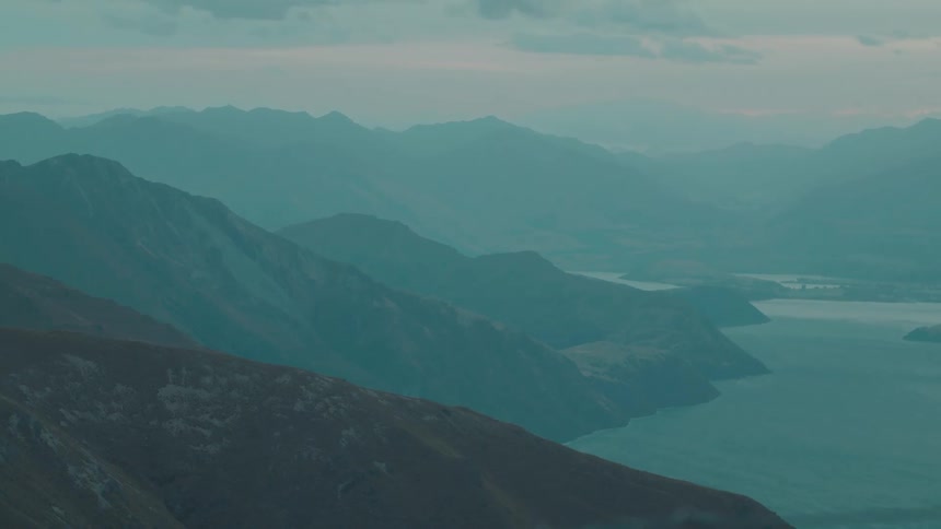 A wide aerial view captures layered mountain ridges descending into a calm lake