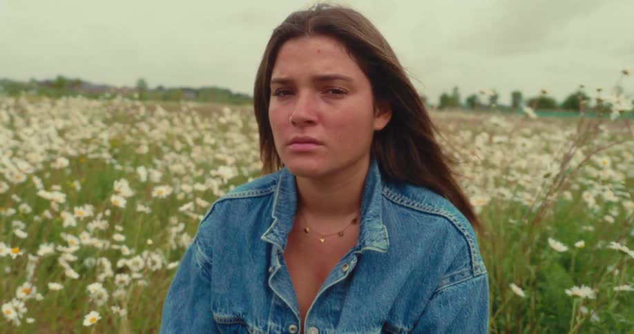 Woman wearing a denim jacket sits in a field of wildflowers on a windy overcast day