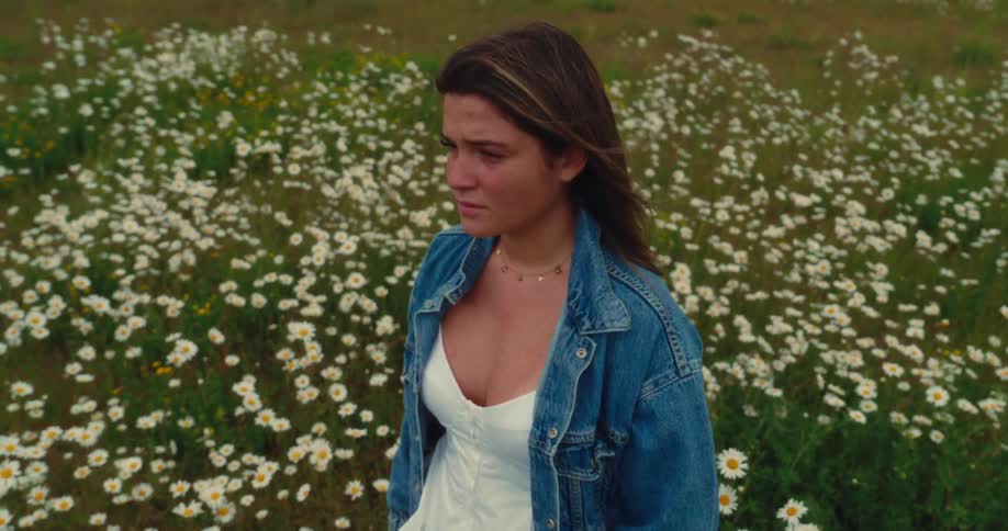 A young woman stands in a field of daisies
