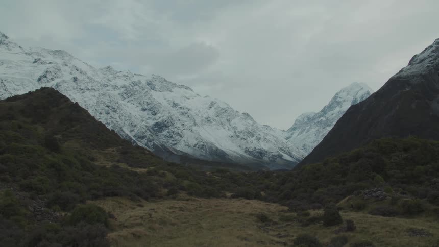 Snowcapped mountains tower over a quiet rugged valley under a cloudy sky