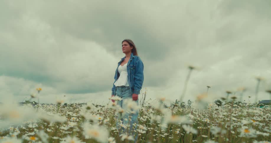 Woman in a denim outfit in a field with daisies on a cloudy day