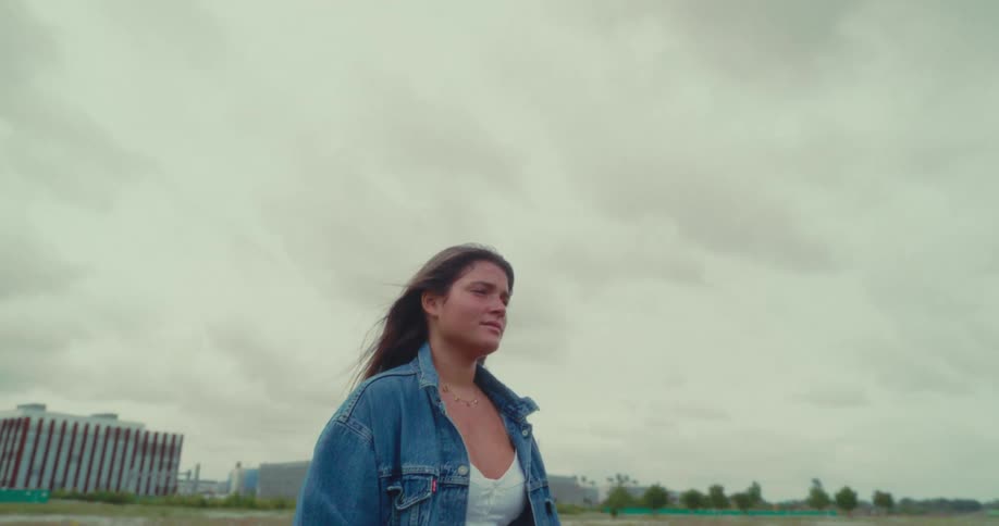 A woman walking on a cloudy day wearing a jean jacket with a soft breeze blowing her hair
