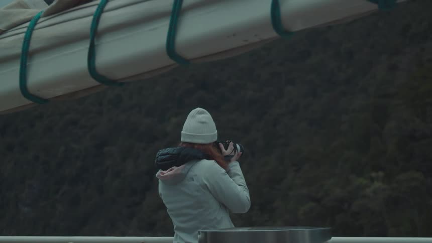 A woman takes pictures of the mountains as she rides on a boat