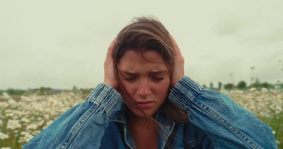 A young woman holds her head in distress while standing in a daisy field