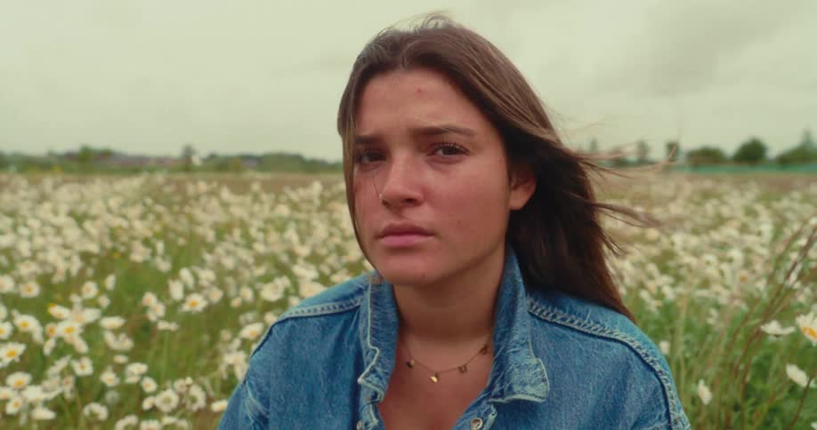 Woman wearing a denim jacket sits in a field of flowers on a windy overcast day