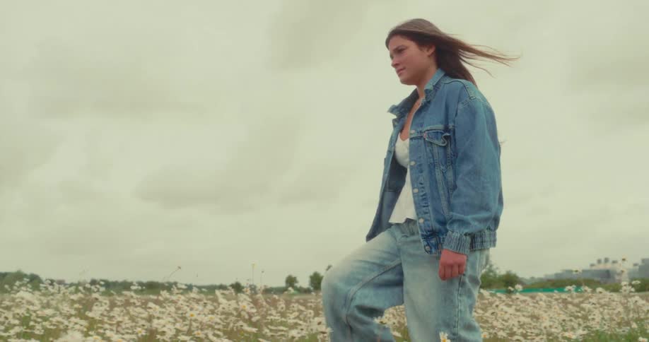 Woman wearing denim walks through a field of wildflowers on an overcast day
