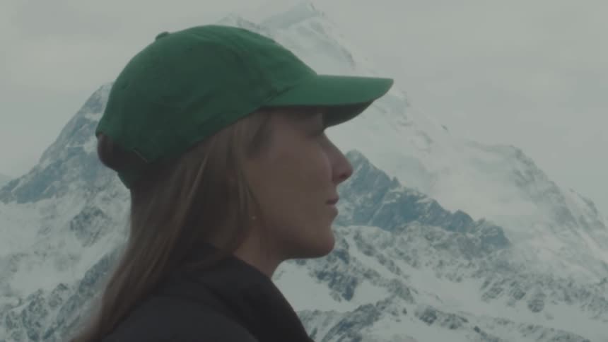 A woman in a green cap looks out pensively at snowcovered mountains