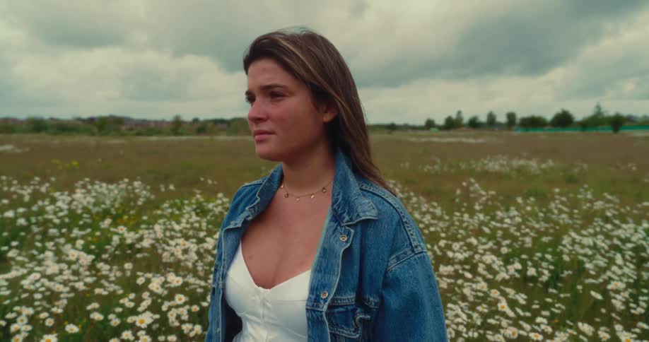 Young woman stares contemplatively while standing among wildflowers in a meadow during the day