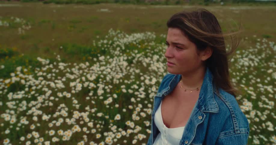 A girl stands in the flowers on a windy day