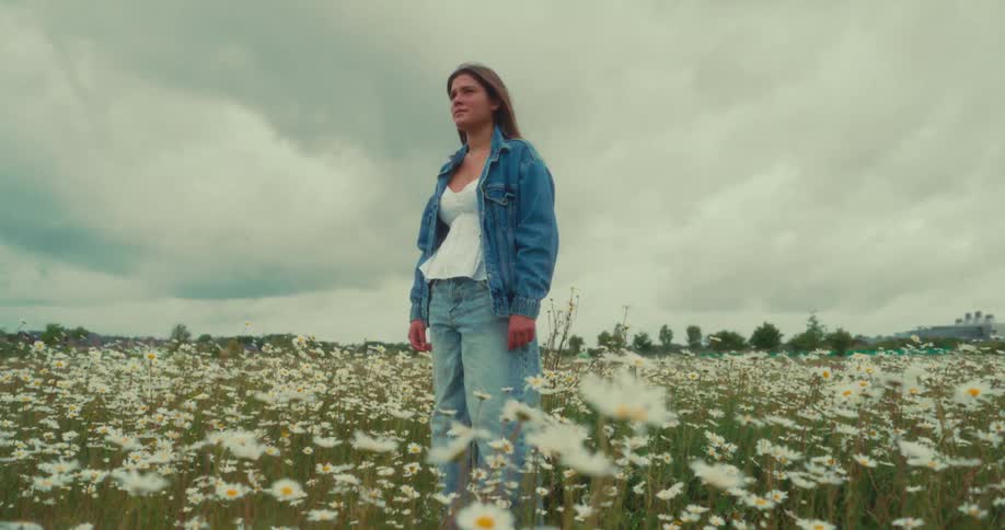 Woman wearing denim stands in a field of wildflowers on an overcast day