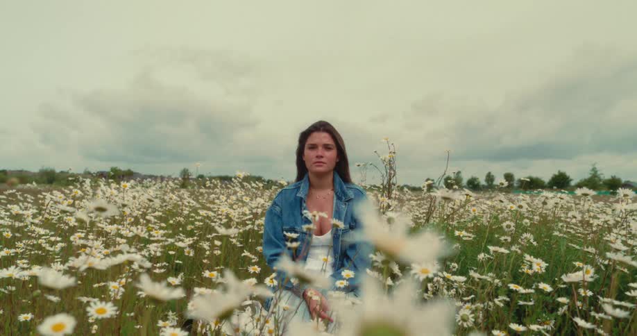 Woman contemplates while kneeling among wildflowers in the meadow during the day