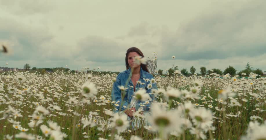 Woman stares contemplatively as she kneels among swaying wildflowers in the meadow